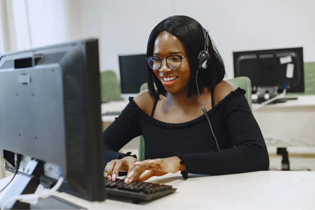 A lady on headphones and a pair of glasses typing on a computer